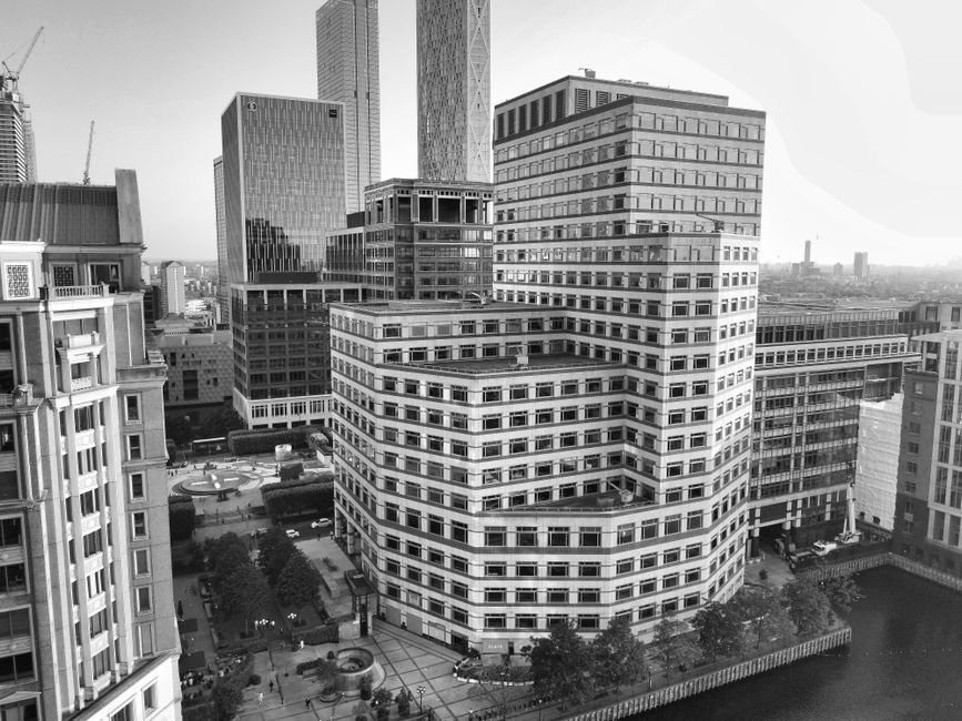 A tall, modern commercial skyscraper viewed from ground level looking upward, with a grid-like pattern of windows on its grey facade. The building’s rectangular shape extends towards a cloudy overca